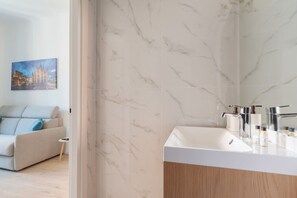 A modern bathroom with a marble wall, a white sink, and a mirror. - GuestHost - Comfortable 30m2 studio, perfect for 2, located on the second floor of a building with lift.The apartment is located in the Ca' Granda - Prato Centenaro area, located in Municipality 9 north of Milan, a well-connected residential area (M5 Ca' (Milan)