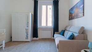 A room with a sofa, a table, a cabinet, a window with curtains, and a painting on the wall. - GuestHost - Comfortable 30m2 studio, perfect for 2, located on the second floor of a building with lift.The apartment is located in the Ca' Granda - Prato Centenaro area, located in Municipality 9 north of Milan, a well-connected residential area (M5 Ca' (Milan)