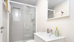 Et moderne badeværelse med bruseniche, et hvidt toilet og en vask med et spejl over.