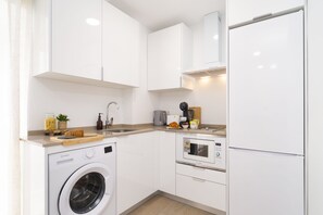 A modern kitchen with a washing machine, microwave, and refrigerator.