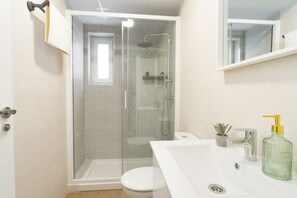 A modern bathroom with a glass-enclosed shower, a white toilet, and a sink with a soap dispenser. - Apartamento Don José 2Izq (Malaga)