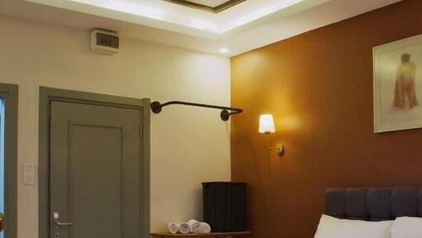 A hotel room with a bed, a bedside lamp, a wall-mounted shelf with towels, and a door. - PeraHomes De (İstanbul)