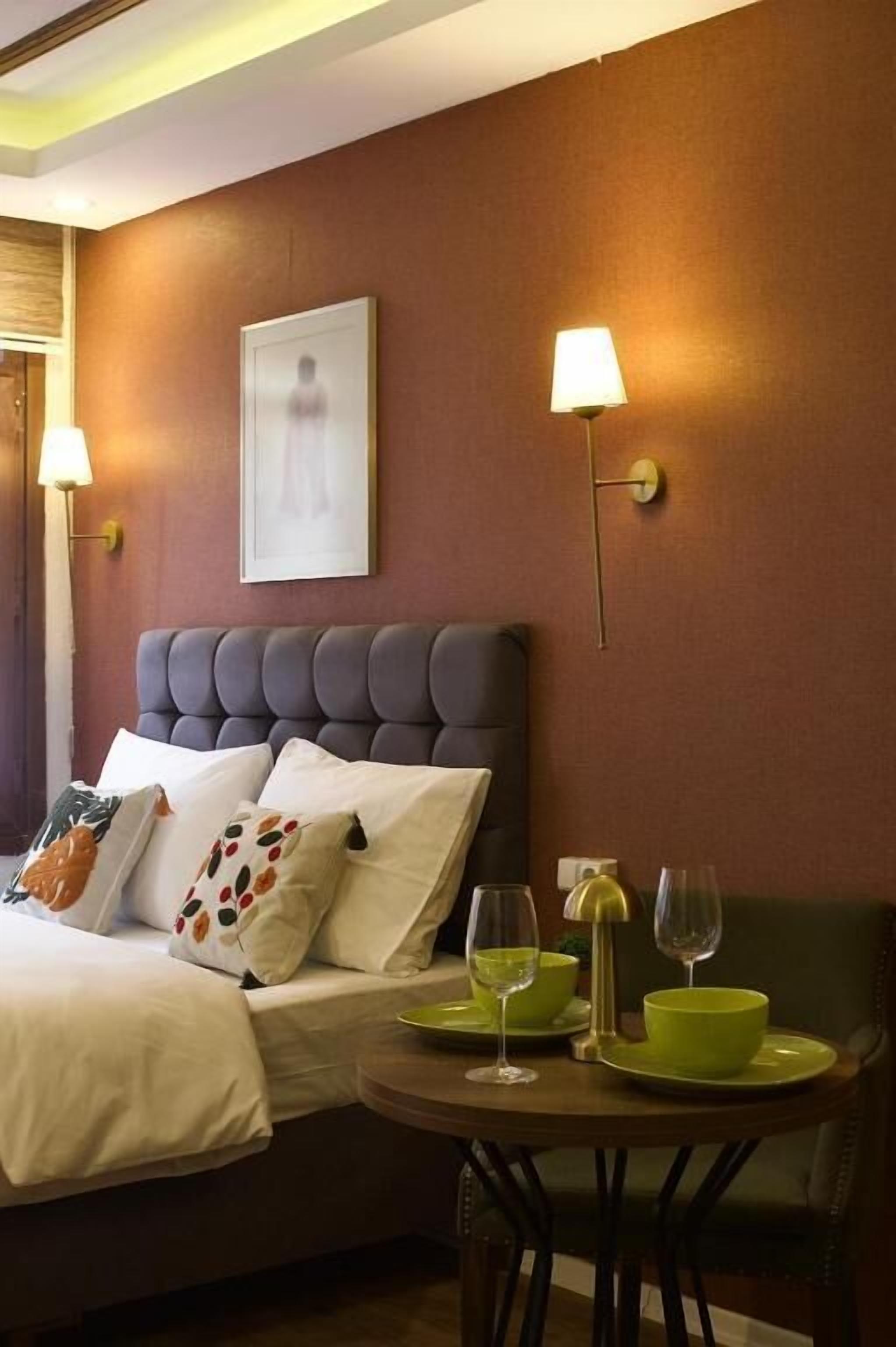 Una habitación de hotel con cama, mesitas de noche, un cuadro enmarcado y una lámpara de pared.
