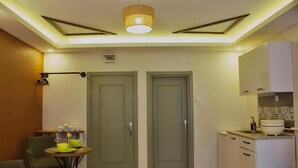 A compact hotel room with a kitchenette, a dining area with a table and chairs, and two doors. - PeraHomes De (İstanbul)