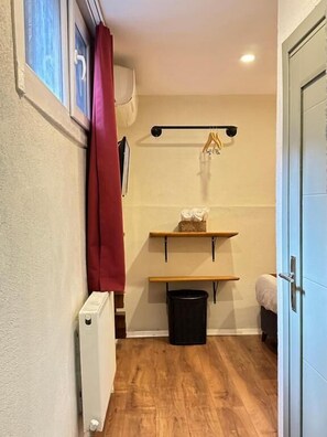 A narrow room with a radiator, a black trash bin, wooden flooring, and a door. - PeraHomes De (İstanbul)