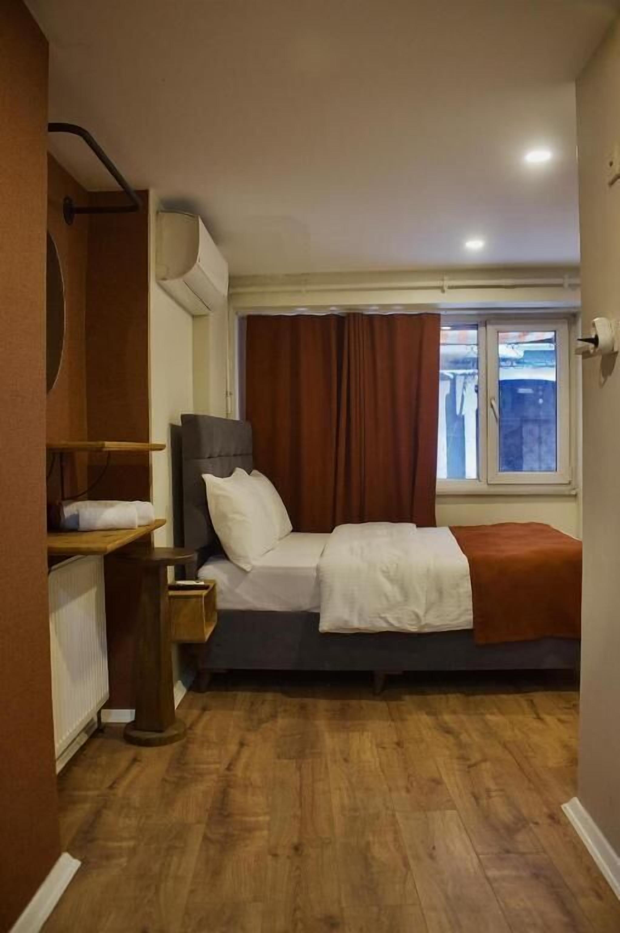 Un dormitorio pequeño con cama, mesita de noche, ventana con cortinas y radiador.
