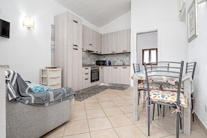 Una cucina compatta con zona pranzo, un divano e una TV fissata al muro.