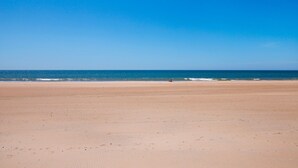 Una extensa playa arenosa, cielo azul despejado y mar tranquilo.