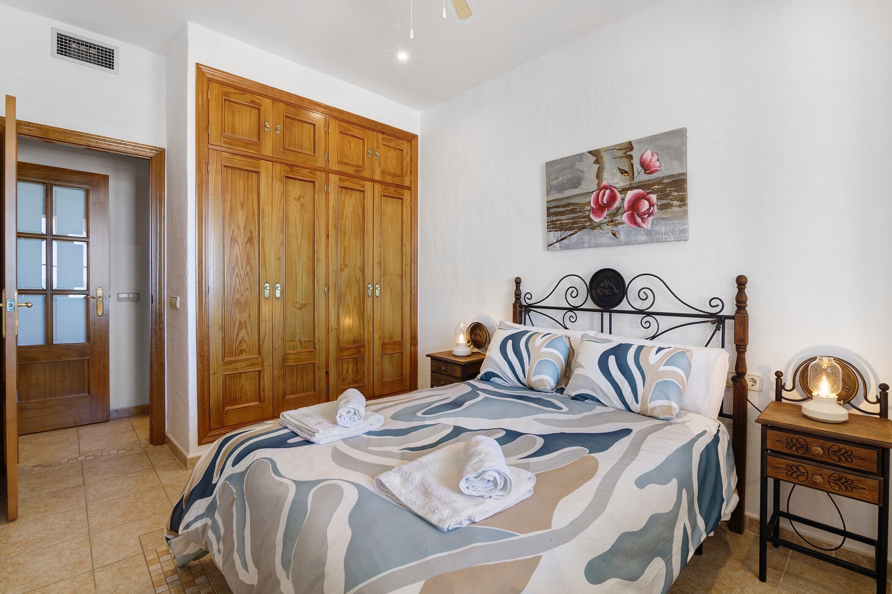 Une chambre à coucher avec un lit, une armoire en bois, une table de chevet et un tableau accroché au mur.