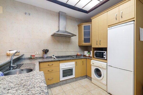 A kitchen with granite countertops, a stainless steel range hood, a built-in oven, a microwave, and a washing machine. - Beachfront House in Matalascañas with Sea Views (Matalascañas)