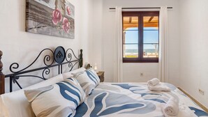 Un dormitorio con cama, un cuadro, una ventana con cortinas y vista al mar.