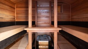 Un sauna avec des bancs en bois, un élément chauffant central et une bouche d’aération au plafond.
