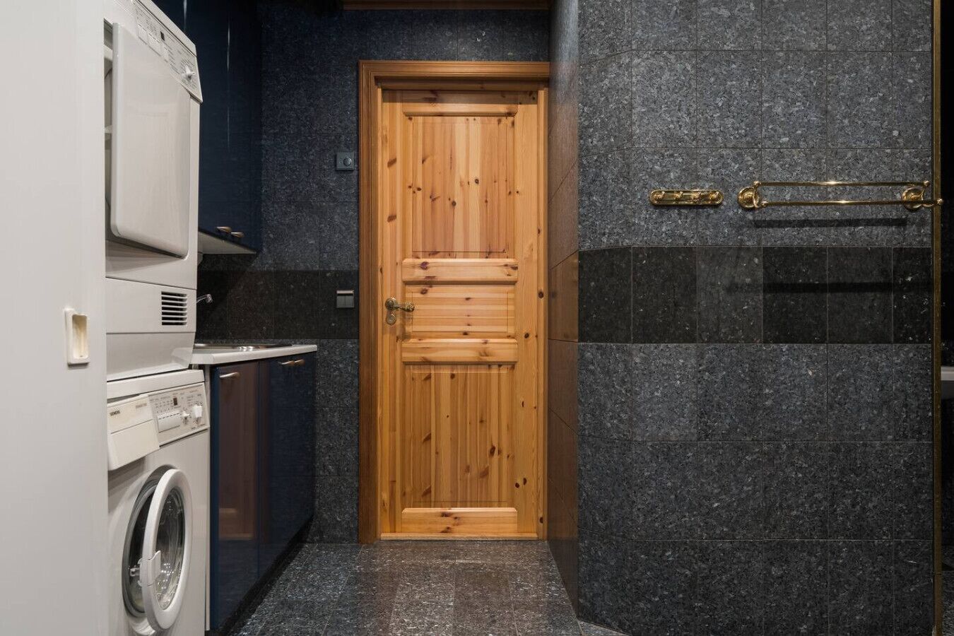 A compact kitchen with a washing machine, a wooden door, and dark granite countertops.