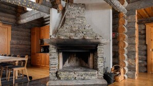 Une cheminée en pierre avec un manteau en bois, un coin repas avec une table et des chaises en bois, et une cuisine avec des armoires en bois.