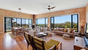 A spacious living area with a dining table, sofas, and a view through large windows.