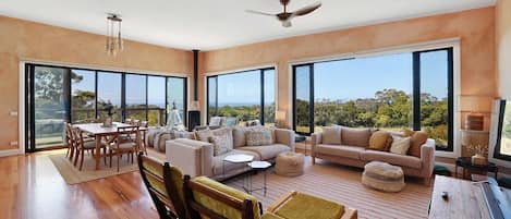 A spacious living area with a dining table, sofas, and a view through large windows.