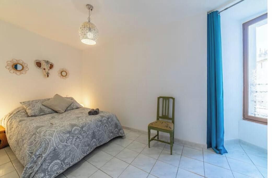 Un dormitorio con cama, una silla, un ventanal con cortinas y adornos en la pared.