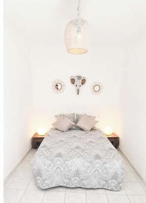 Ein Schlafzimmer mit geblümter Bettdecke, zwei Nachttischlampen, einer Hängelampe und Wanddekoration.