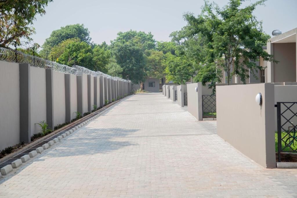 Un largo sendero recto bordeado por altos muros con alambre de púas, que conduce a un edificio con entrada vigilada.