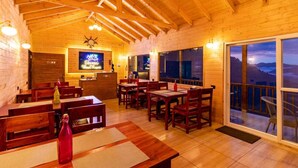 Un intérieur en bois avec des tables et des chaises, un coin bar et de grandes fenêtres offrant une vue dégagée.