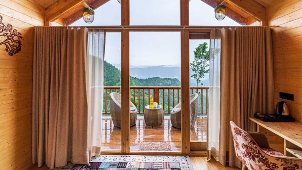 Une cabane en bois dotée d’un balcon, de meubles en osier et offrant une vue sur les montagnes.