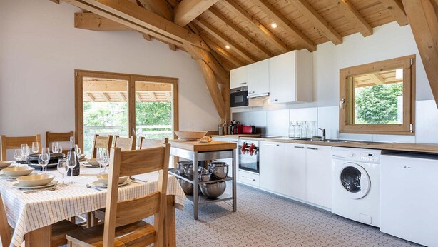 A kitchen with wooden beams, a dining table set for four, and a washing machine. - Chalet in Paradiski With Spa and Mountain Views (Peisey-Nancroix)