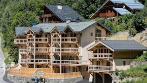 A multi-story lodge with balconies, a stone foundation, and a mountainous backdrop. - Chalet in Paradiski With Spa and Mountain Views (Peisey-Nancroix)