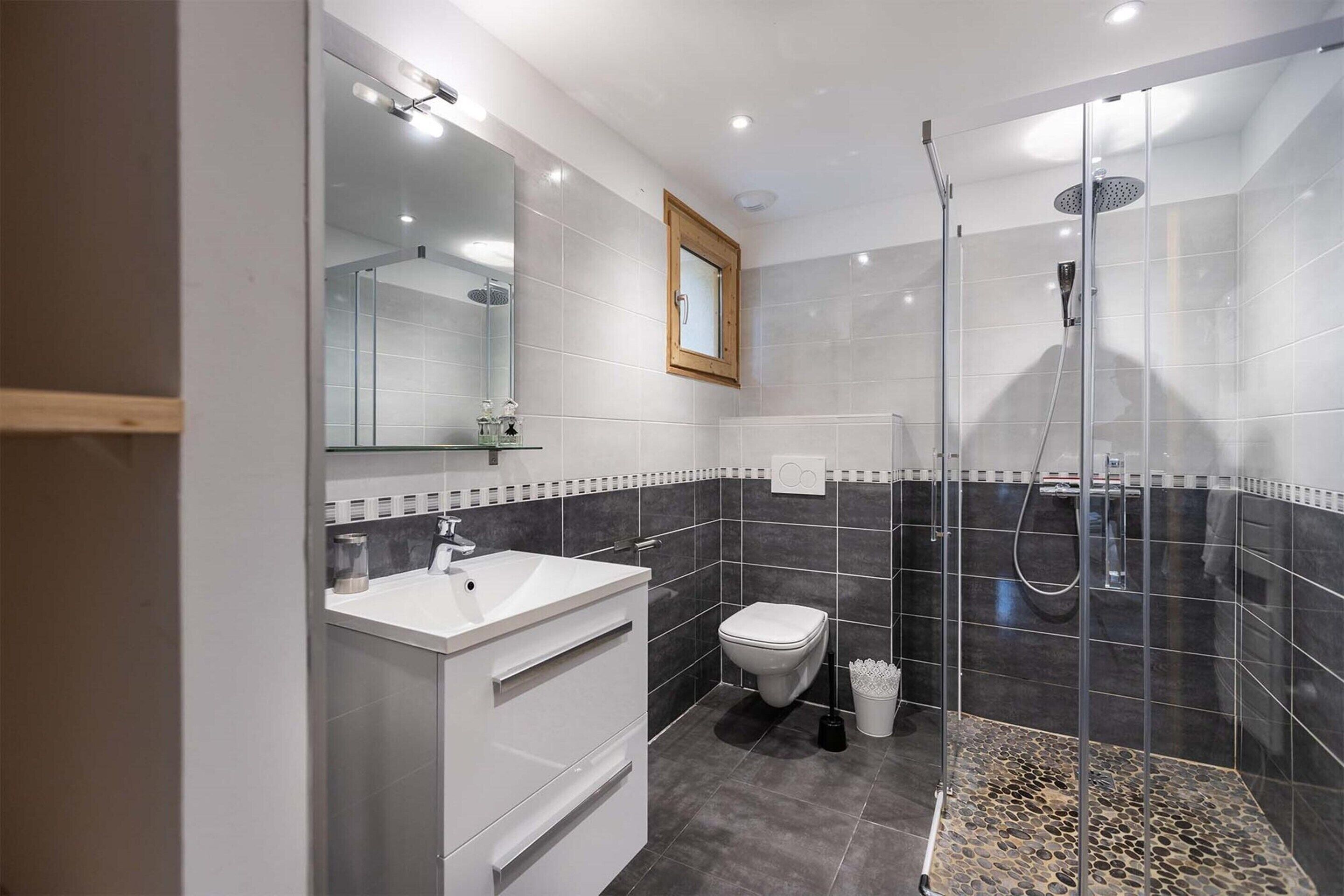 Un baño moderno con ducha de vidrio, lavamanos blanco y retrete.