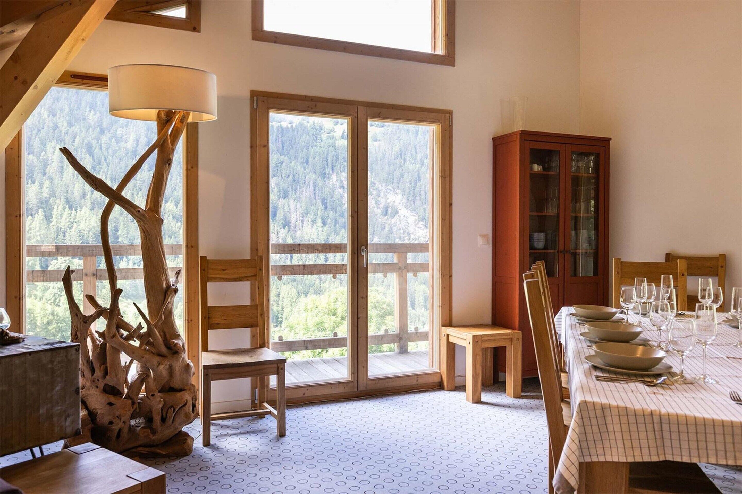 Ein Essbereich mit Tisch für vier Personen, einem Holzschrank und Blick auf einen Wald durch große Fenster.