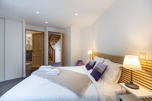 A hotel room with a bed, a nightstand, a lamp, a wooden headboard, and a bathroom visible through an open door. - Chalet in Paradiski With Spa and Mountain Views (Peisey-Nancroix)