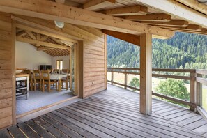 A wooden deck with a dining area and a view of a forested mountain. - Chalet in Paradiski With Spa and Mountain Views (Peisey-Nancroix)