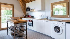 A modern kitchen with white cabinets, a wooden countertop, a built-in oven, a washing machine, and a large window. - Chalet in Paradiski With Spa and Mountain Views (Peisey-Nancroix)