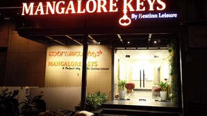 A hotel entrance with a neon sign reading 'MANGALORE KEYS By Bestinn Leisure' and a reception desk visible inside.