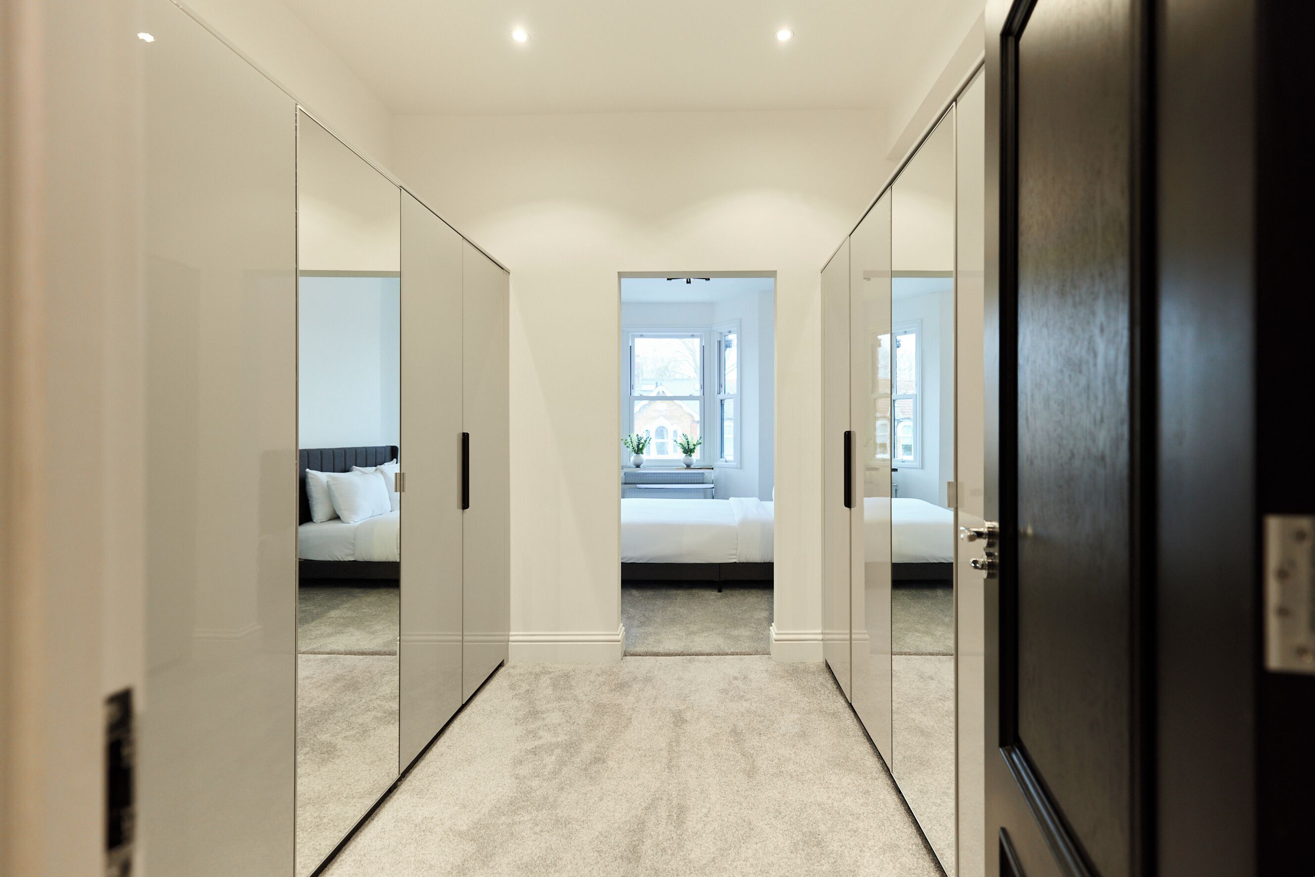 Un pasillo con puertas de armario espejadas que conduce a un dormitorio con cama y ventana.