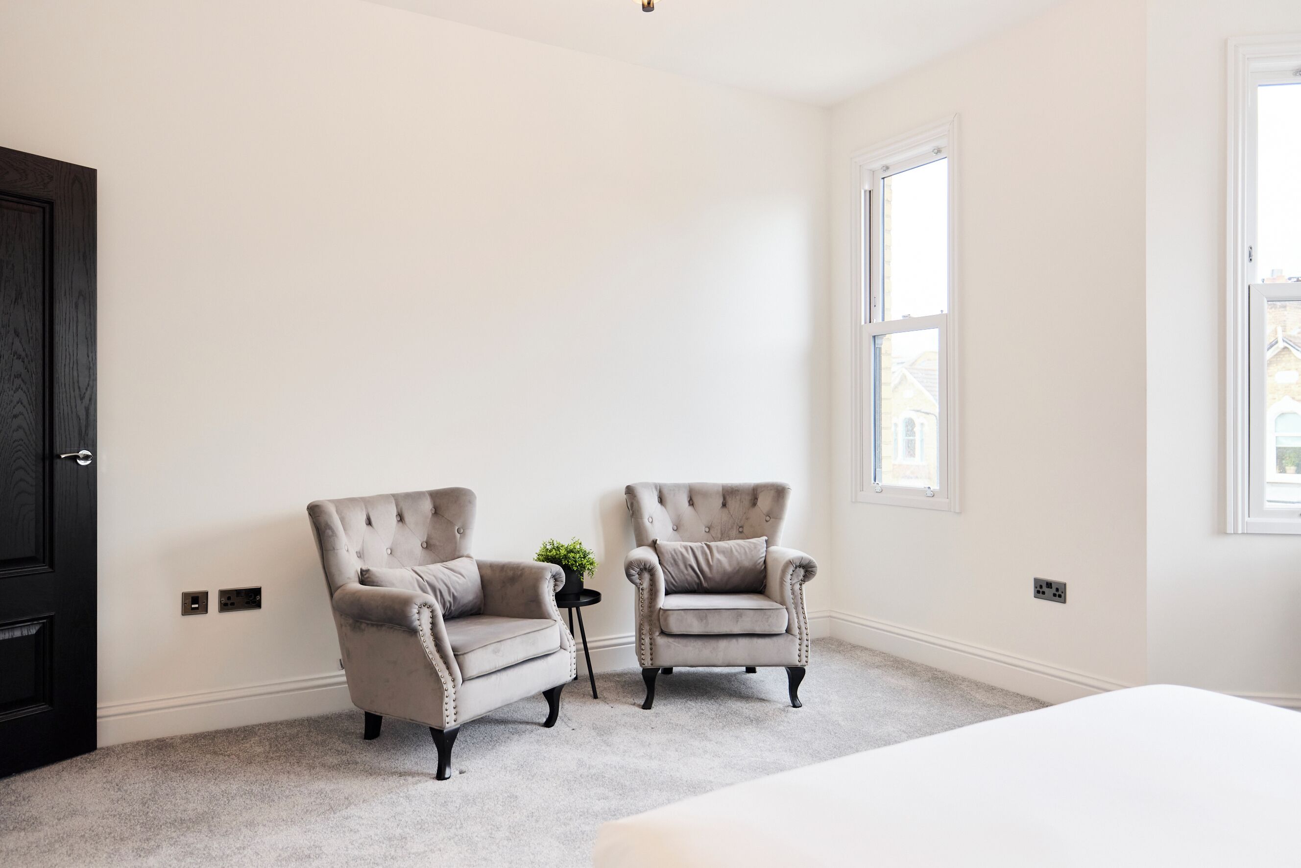 A room with two armchairs, a small table with a plant, and a large window.