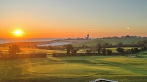 Un campo de golf con una bandera, un faro y un atardecer sobre el océano.