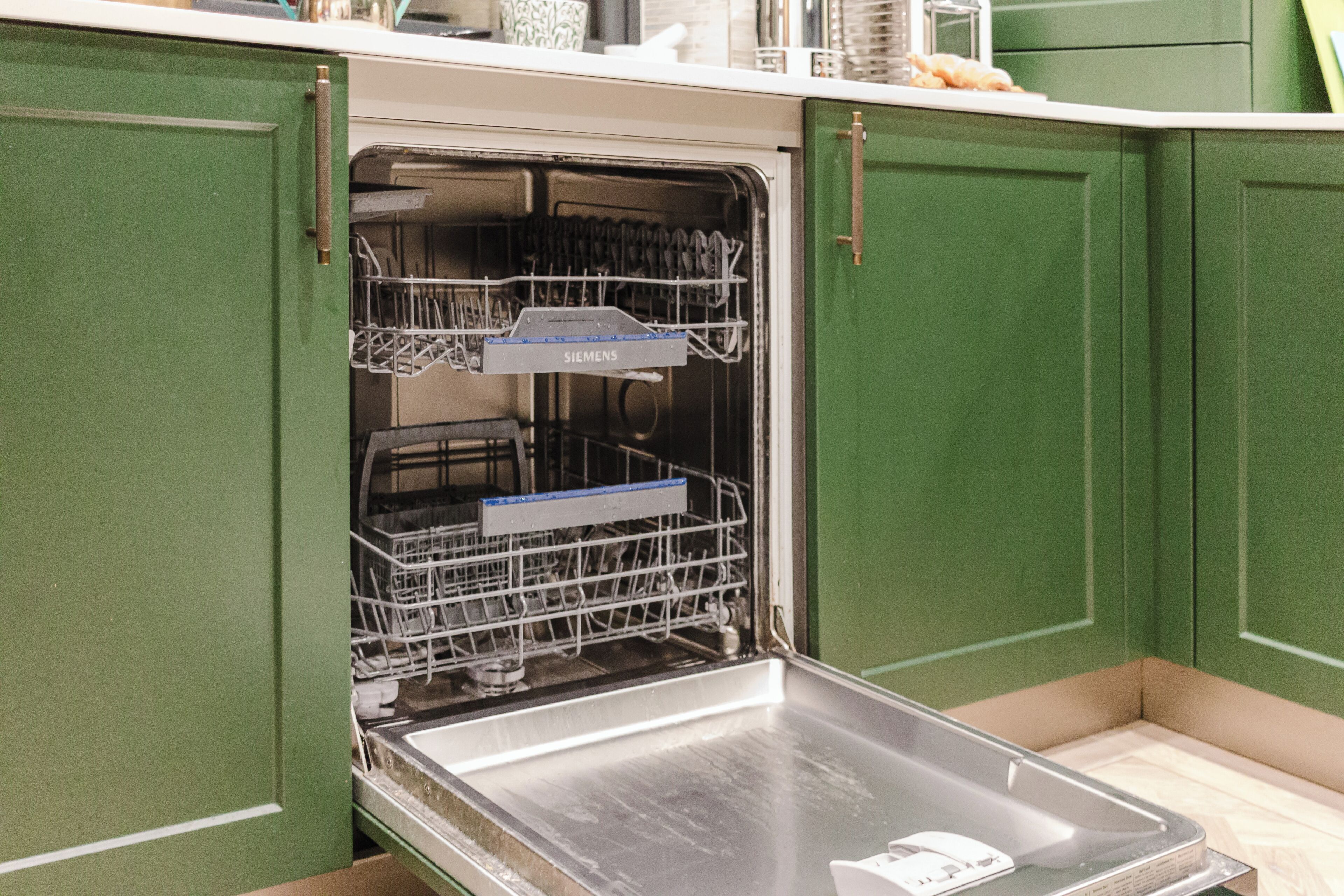 An open dishwasher in a kitchen with green cabinets.