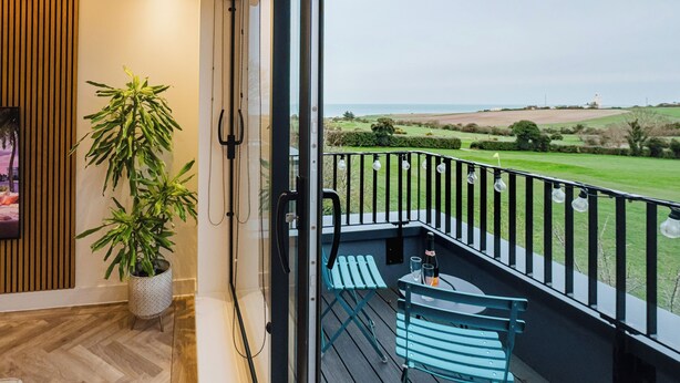 Un balcón con vistas al mar, una planta en maceta y una mesa con sillas.