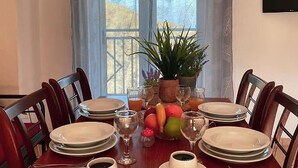 Mesa de jantar posta para quatro pessoas, com pratos, copos e uma tigela de frutas.