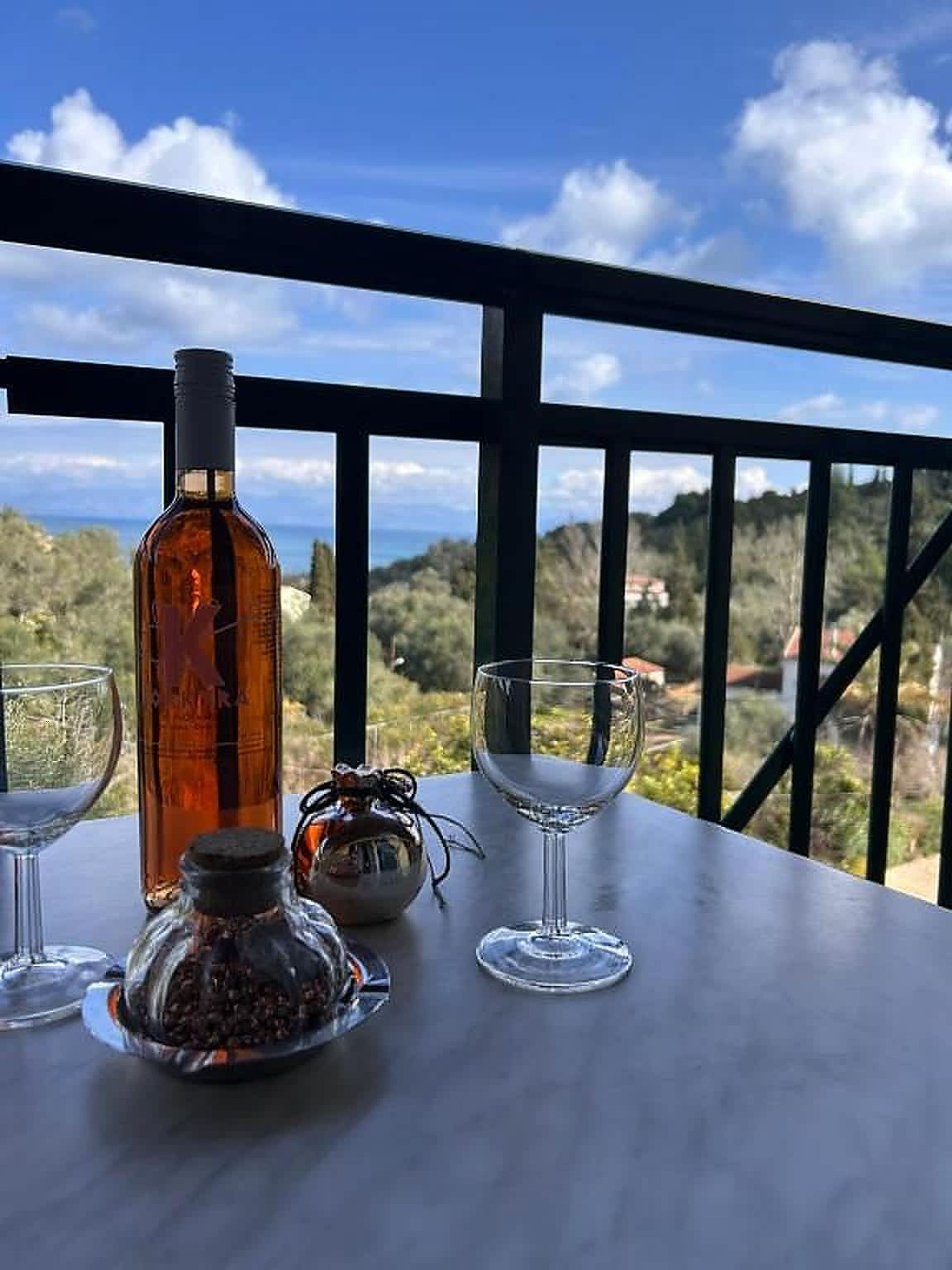 A table with a bottle and two glasses on a balcony with a view.