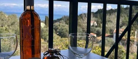A table with a bottle and two glasses on a balcony with a view.