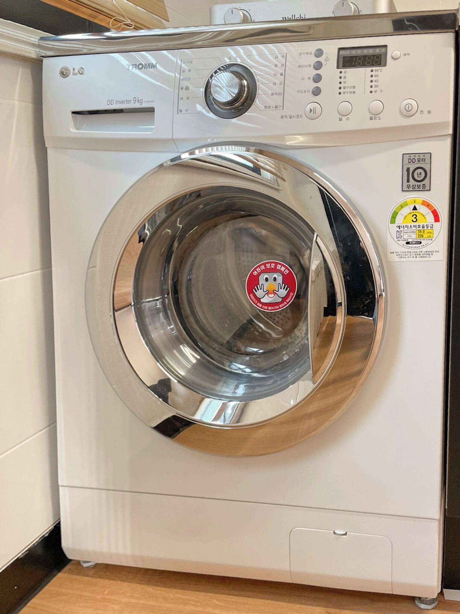 A front-loading LG washing machine with a stainless steel door, control panel, and a sticker indicating energy efficiency.