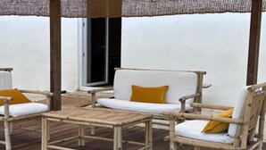A wooden deck with a white sofa and two chairs, a small table, and a woven canopy.