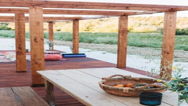 A wooden deck with a table, a basket of fruits, and a blue container.