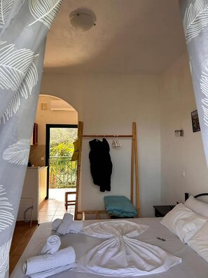 Ein Schlafzimmer mit Bett, Nachttisch, Kleiderhaken und Blick ins Freie.