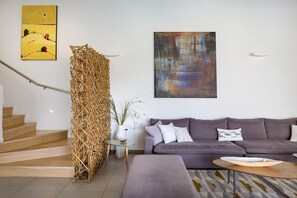 A modern living room with a staircase, a grey sofa, a coffee table, and two artworks on the wall. - Villa Karga (4 bedroom villa) (Almyrida)