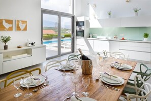 A modern kitchen with a dining area, large windows, and a view of a pool. - Villa Karga (4 bedroom villa) (Almyrida)