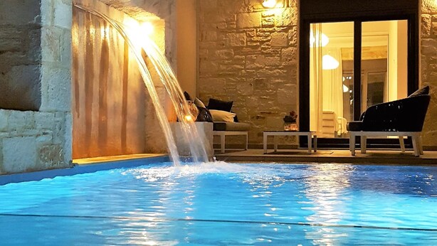 En inomhuspool med ett vattenfall, stenmurar och en balkong med sittplatser.