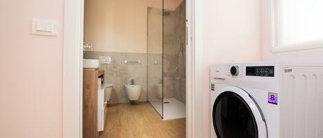 Un baño moderno con cabina de ducha de vidrio, lavadora e inodoro.