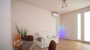 Een moderne woonkamer met een glazen eettafel, twee stoelen, een witte bank en een potplant.